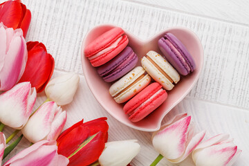Pastel colorful tulips and vibrant macaroons fill a heart-shaped bowl