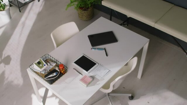 No people top shot of doctors desk in GP clinic, with laptop, digital tablet, blood pressure monitor, thermometer, jar of pills, eye exam torch, couch to side, in morning before patient appointments