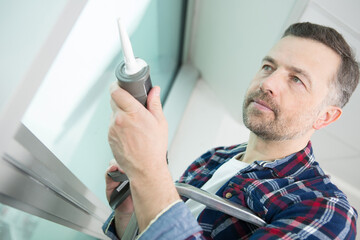construction worker sealing window with caulk indoors