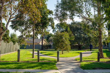 A green outdoor space in a suburban neighborhood park with pedestrian footpaths, wooden bollards and trees. Hoppers Crossing, Melbourne Australia