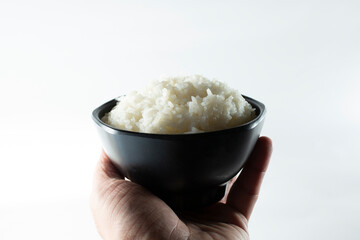 A view of a hand holding a bowl of steamed white rice, against a white background.