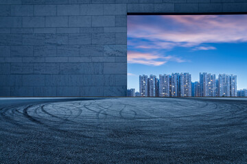Fototapeta premium Asphalt road square and brick wall with city buildings at night. car background.