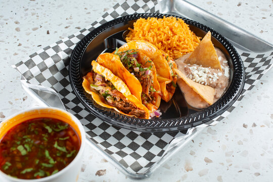 A view of a cup of consomme with beef birria tacos.