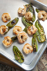 A top down view of roasted shrimp and jalapeno peppers on a baking sheet.