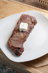 A view of a cooked strip steak with a slice of butter on top.