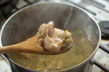 A view of a wooden spoon scooping some chicken from a stockpot of pozole verde.