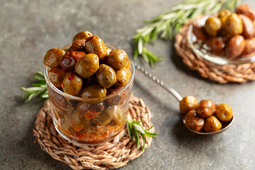 Spicy olives in a glass bowl on a stone table.