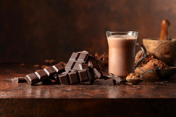 Pieces of bitter chocolate and glass of cocoa drink on a brown table.