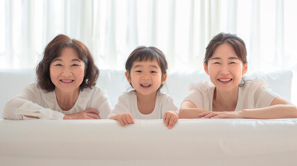 Three generations of women, grandmother, mother, and daughter, smiling together on a white couch