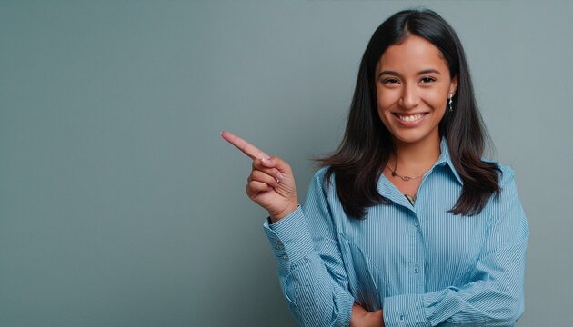 Happy young smiling professional business woman wearing blue shirt looking at camera pointing finger away at copy space showing aside presenting advertising offer standing isolated at gray background