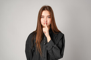 Smiling Young Woman Posing With Finger on Lips Against Grey Backdrop