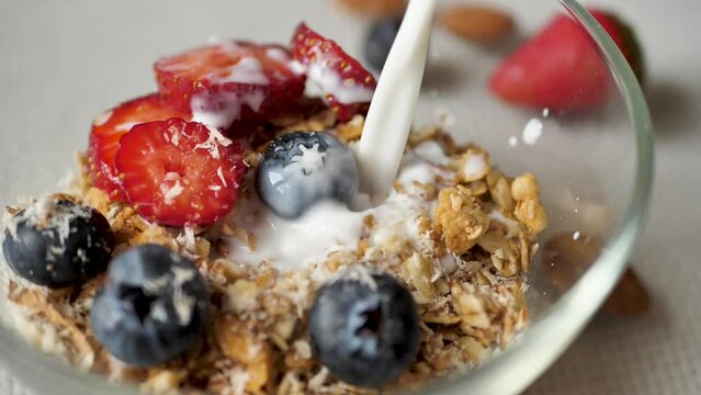 Close-up of pouring milk into a plate with strawberries, blueberries and granola for a nutritious healthy breakfast. Pour a slow stream of milk into the granola with berries. Healthly food