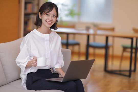 ソファでノートパソコンを操作する30代女性