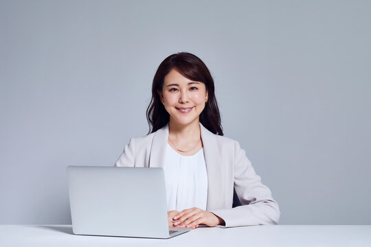 カメラ目線のスーツを着た女性とノートパソコン