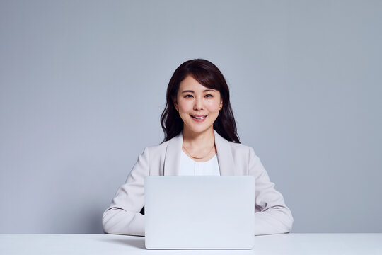 カメラ目線のスーツを着た女性とノートパソコン