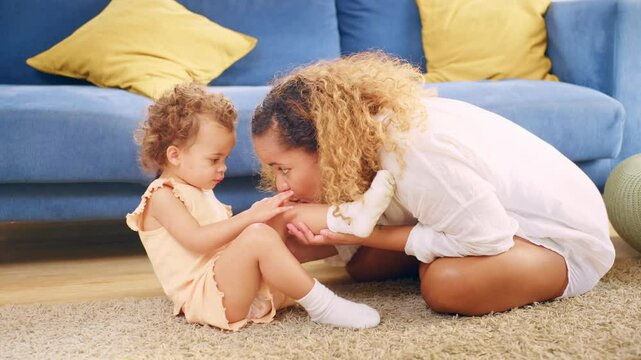 African American mother blowing wound on knee of baby girl in house. 