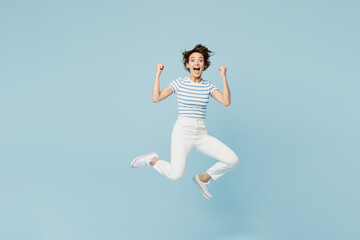 Fototapeta premium Full body young woman wears striped t-shirt casual clothes jump high doing winner gesture celebrate clenching fists isolated on plain pastel light blue background studio portrait. Lifestyle concept.