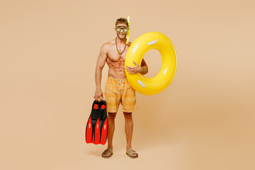 Full body young sexy man wear yellow shorts swimsuit hat diving mask relax rest near hotel pool hold rubber ring flippers isolated on plain beige background. Summer vacation sea rest sun tan concept. © ViDi Studio