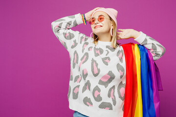 Young happy lesbian woman wear pink animal clothes hold striped rainbow flag on shoulder look aside on area mockup isolated on plain purple background studio. Pride day June month love LGBTQ concept.