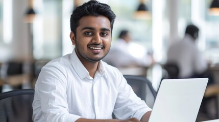 Obraz premium a young smiling indian businessman is sitting at his laptop in the office