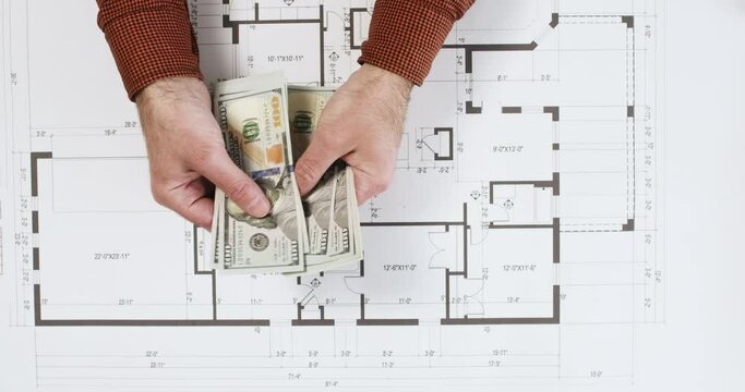 Man pays for builders work over building floor plan upper view. Customer counts dollar bills for contractor on printout drawing in office