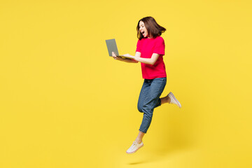 Full body side view smart young IT woman in pink t-shirt casual clothes jump high hold use work on laptop pc computer run isolated on plain yellow orange background studio portrait Lifestyle concept