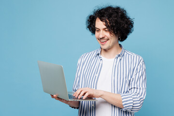 Young smiling happy cheerful smart IT man wear shirt white t-shirt casual clothes hold use work on laptop pc computer isolated on plain pastel blue cyan background studio portrait. Lifestyle concept.