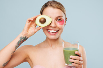Half naked topless young woman with nude make up wearing patch cover eye with avocado drink green...