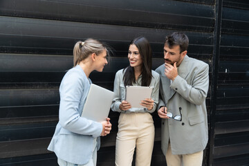 Group of successful young business people, leaders in marketing and motivation, stand in front of office building and consult before a meeting with employees. HR communication in companies concept