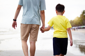 Fototapeta premium Cheerful happy Asian father and son hold their together and walk along the beach.