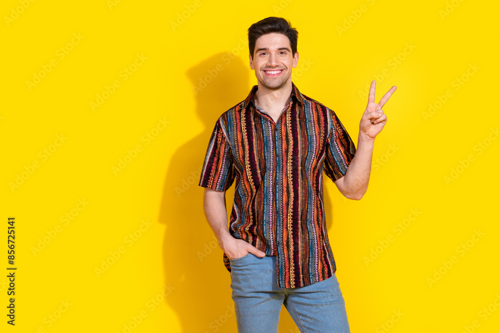 Wall mural Photo of nice young man show v-sign wear shirt isolated on yellow color background