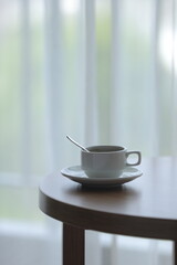 A white mug sits atop a wooden table next to a bright window, invitingly filled with tea drink. Concept Cozy Indoor Table.