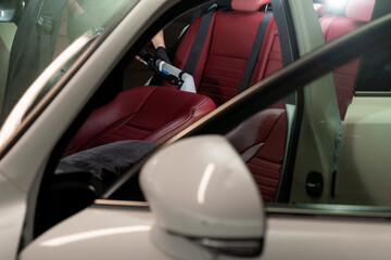 Removing dirt from car seat with the help of special hoover nozzle. Detailing auto seat using vacuum extractor.