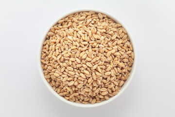Organic Wheat Grains (Triticum) or Caryopsis Fruits, in a white ceramic bowl. Isolated on a gray background. Top View