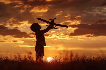 Isolated black silhouette of a young Caucasian boy playing toy plane on grassy summer hill. Dreaming big dreams and setting big goals for the future.