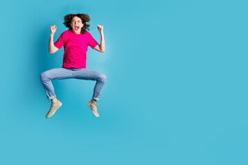 Full size photo of nice young man jump raise fists empty space wear t-shirt isolated on blue color background
