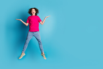 Full size photo of nice young man jump hold empty space vs wear t-shirt isolated on blue color background