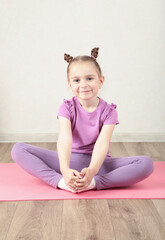 Fototapeta premium Charming little girl is smiling while doing yoga. Vertical photo