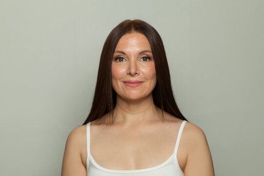 Mid adut brunette woman in white underwear looking at camera on grey background. Skin care, cosmetology, facial treatment concept