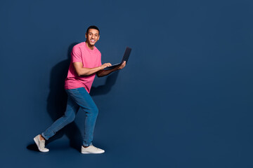 Full body length photo of young man walking using computer working remote ai developer isolated on dark blue color background