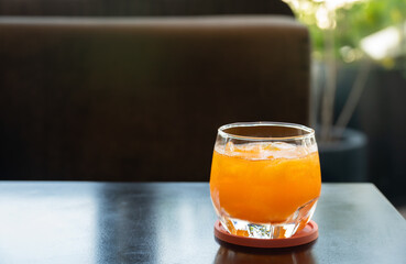 Close-up of orange drink with ice, served in a clear glass placed on wooden table with ambient natural light.