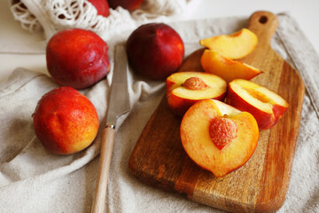Ripe cut peaches on a wooden board and a linen napkin next to a knife and string bag on a light background