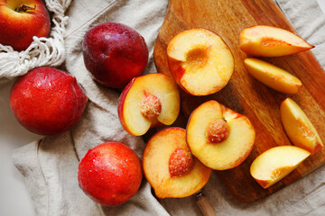 Ripe cut peaches on a wooden board and a linen napkin next to a string bag on a light background