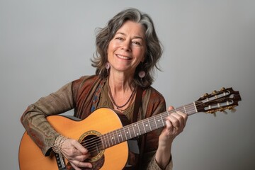 Fototapeta premium Portrait of a cheerful caucasian woman in her 50s playing the guitar isolated on blank studio backdrop