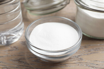 Baking soda in bowl and glass jar on wooden table, closeup