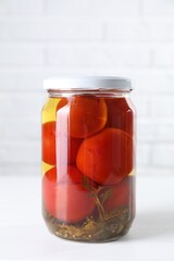 Tasty pickled tomatoes in jar on white table
