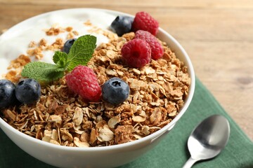 Tasty granola with berries and yogurt in bowl on wooden table, closeup
