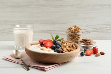 Tasty granola with berries and yogurt in bowl on white table