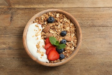 Tasty granola with berries, almond and yogurt in bowl on wooden table, top view