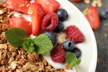 Tasty granola with berries and yogurt in bowl on table, closeup